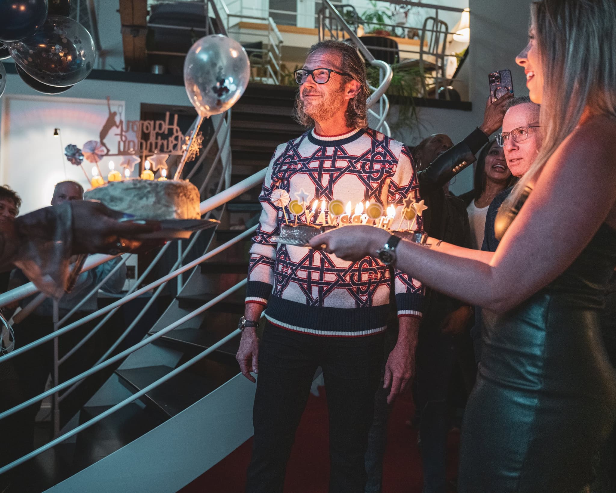 Birthday boy presented with a sparkler-lit cake, crowd cheering in background