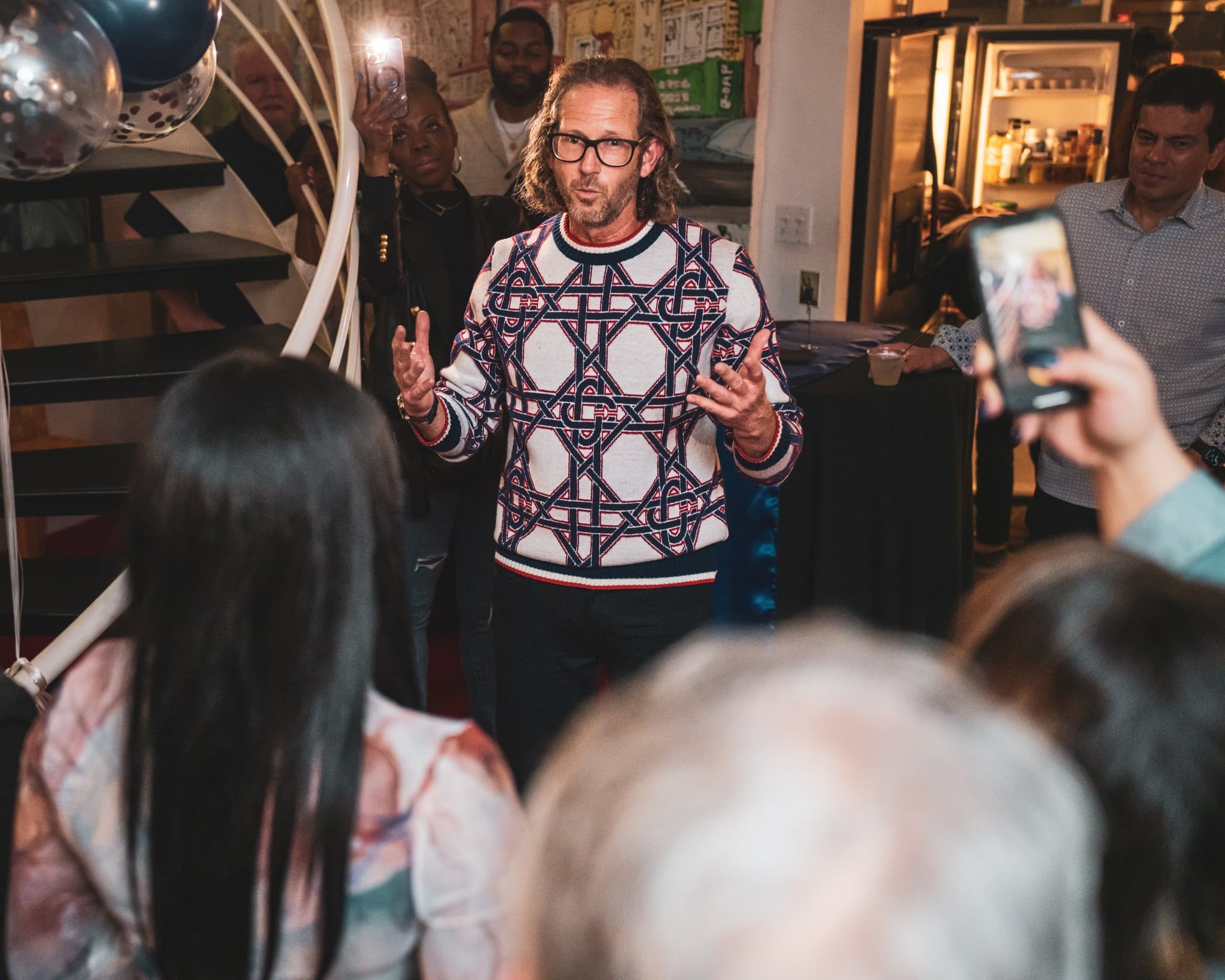 The birthday honoree giving a heartfelt speech to a gathered crowd of guests who are filming on their phones