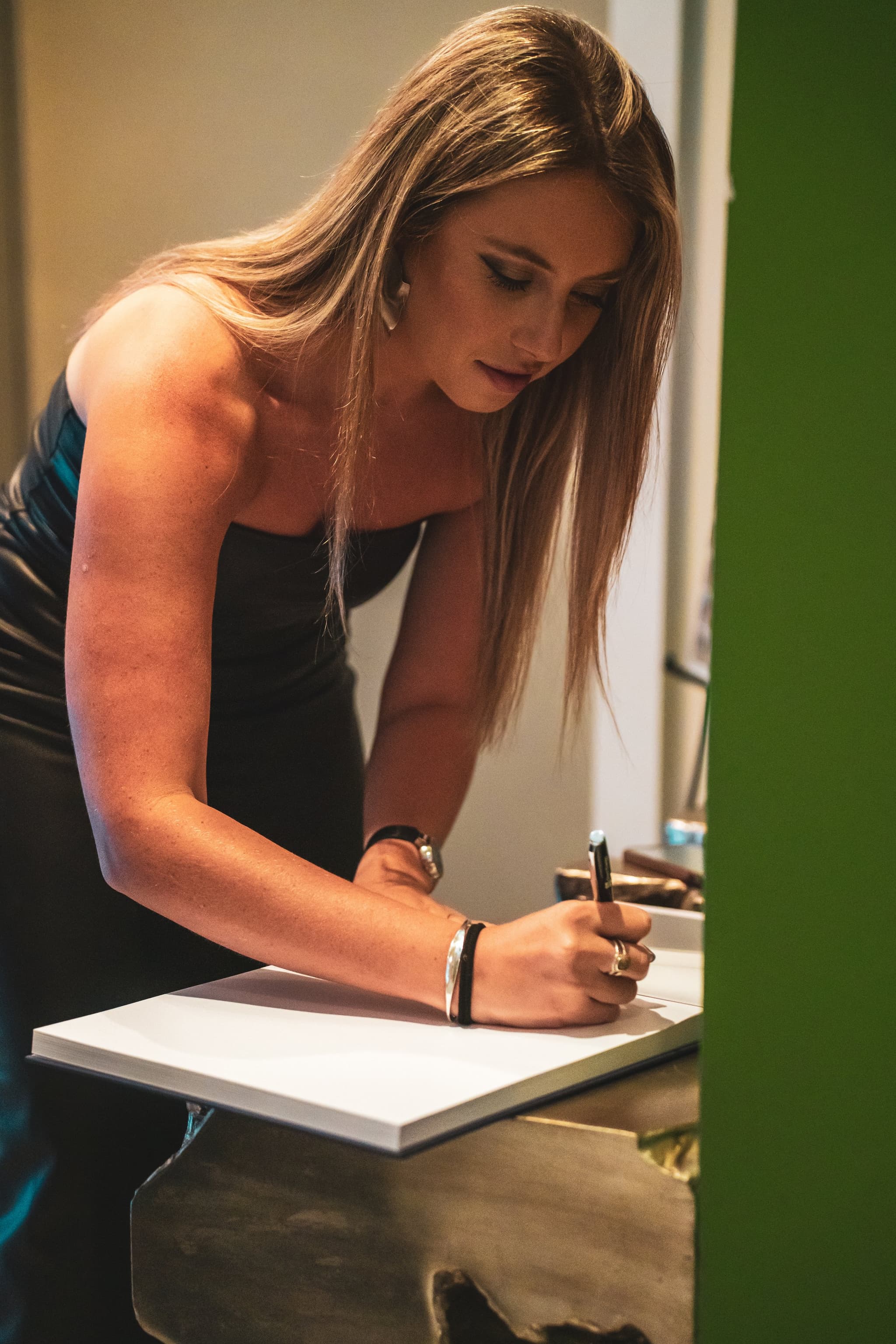 A guest leaning over a table to sign the birthday guestbook, captured in warm intimate light