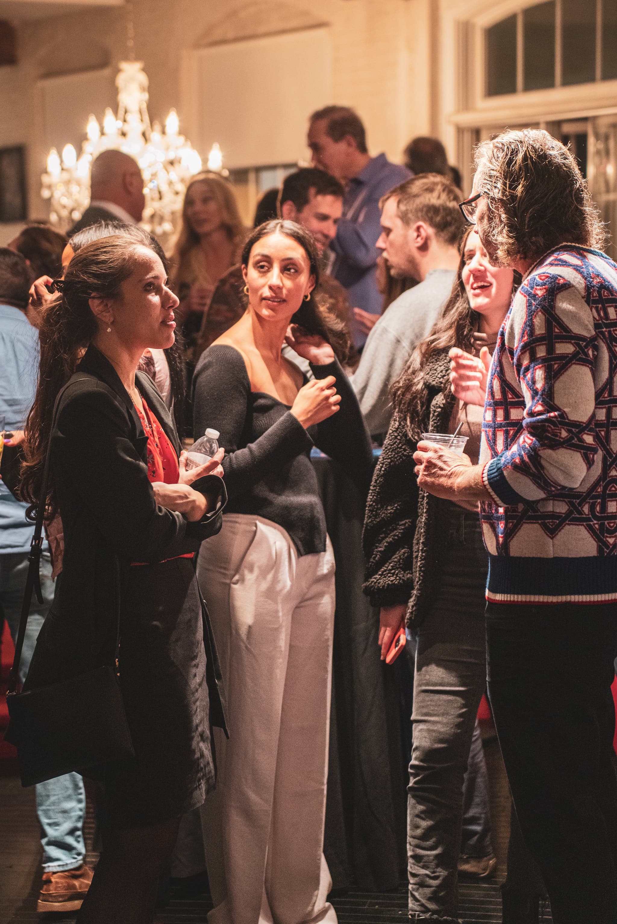 A group of women laughing and mingling together in a warmly lit room filled with birthday party guests