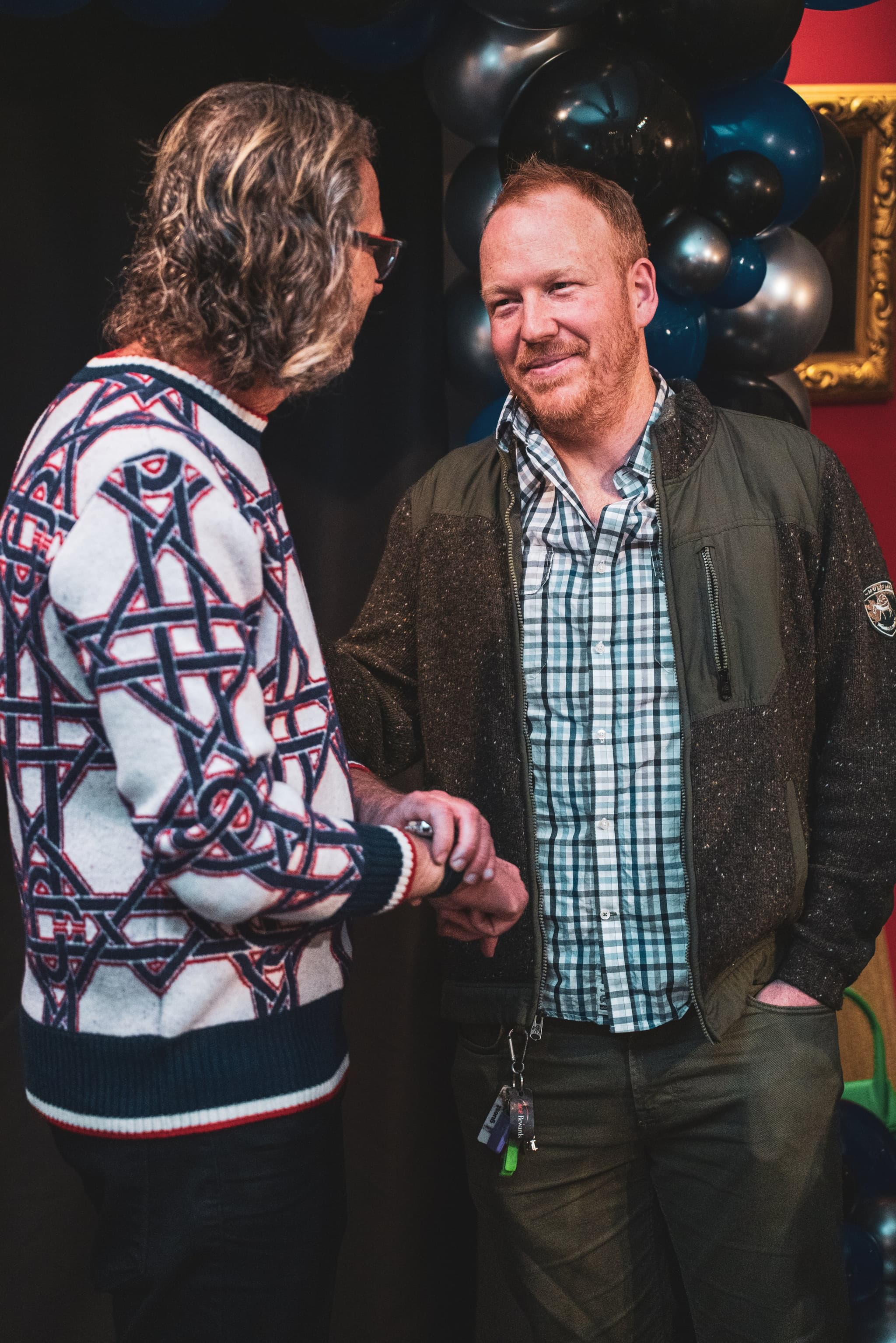 Two guests warmly shake hands in front of a balloon arch at the 60th birthday celebration