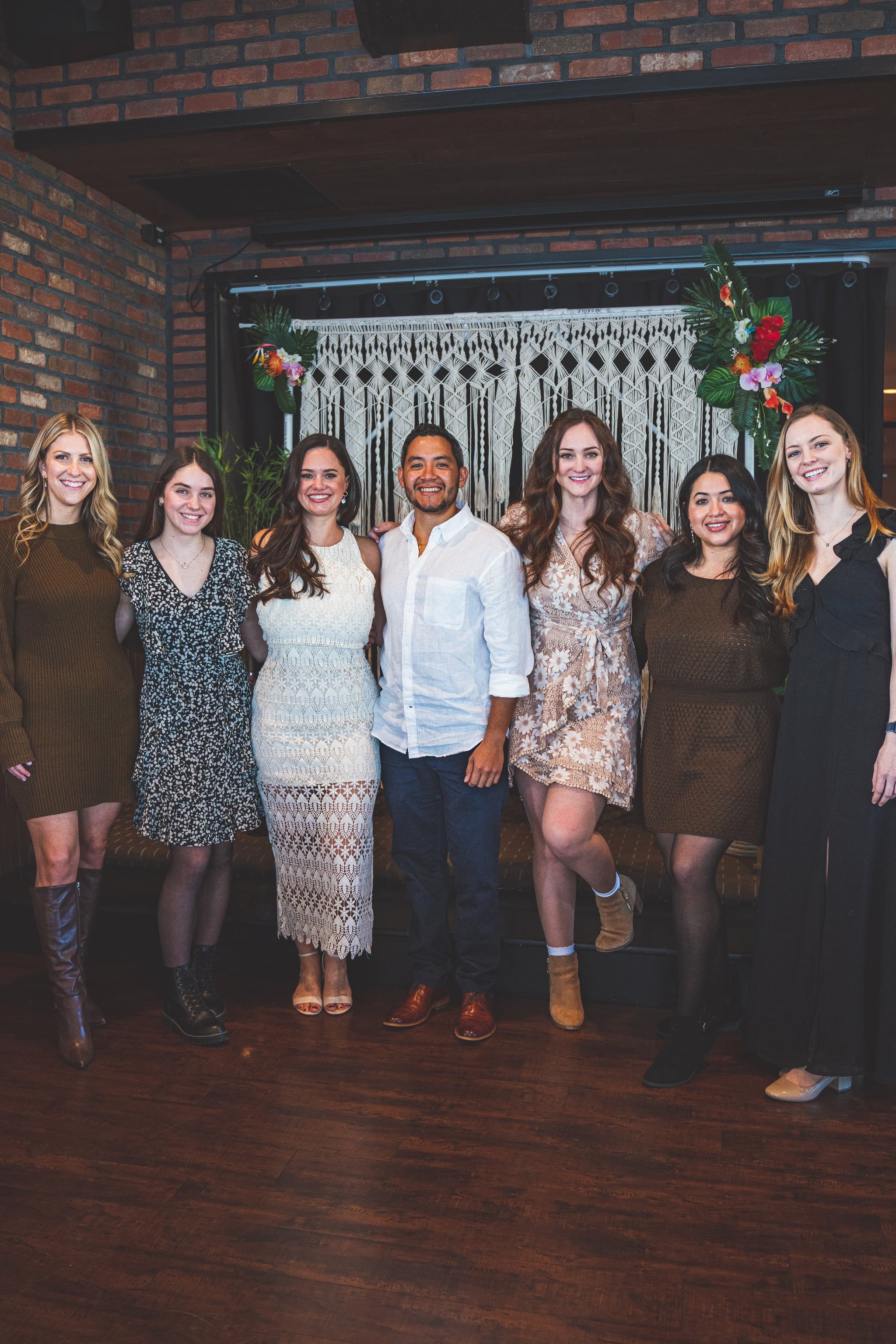 Group of guests posing in front of macrame and tropical floral arch