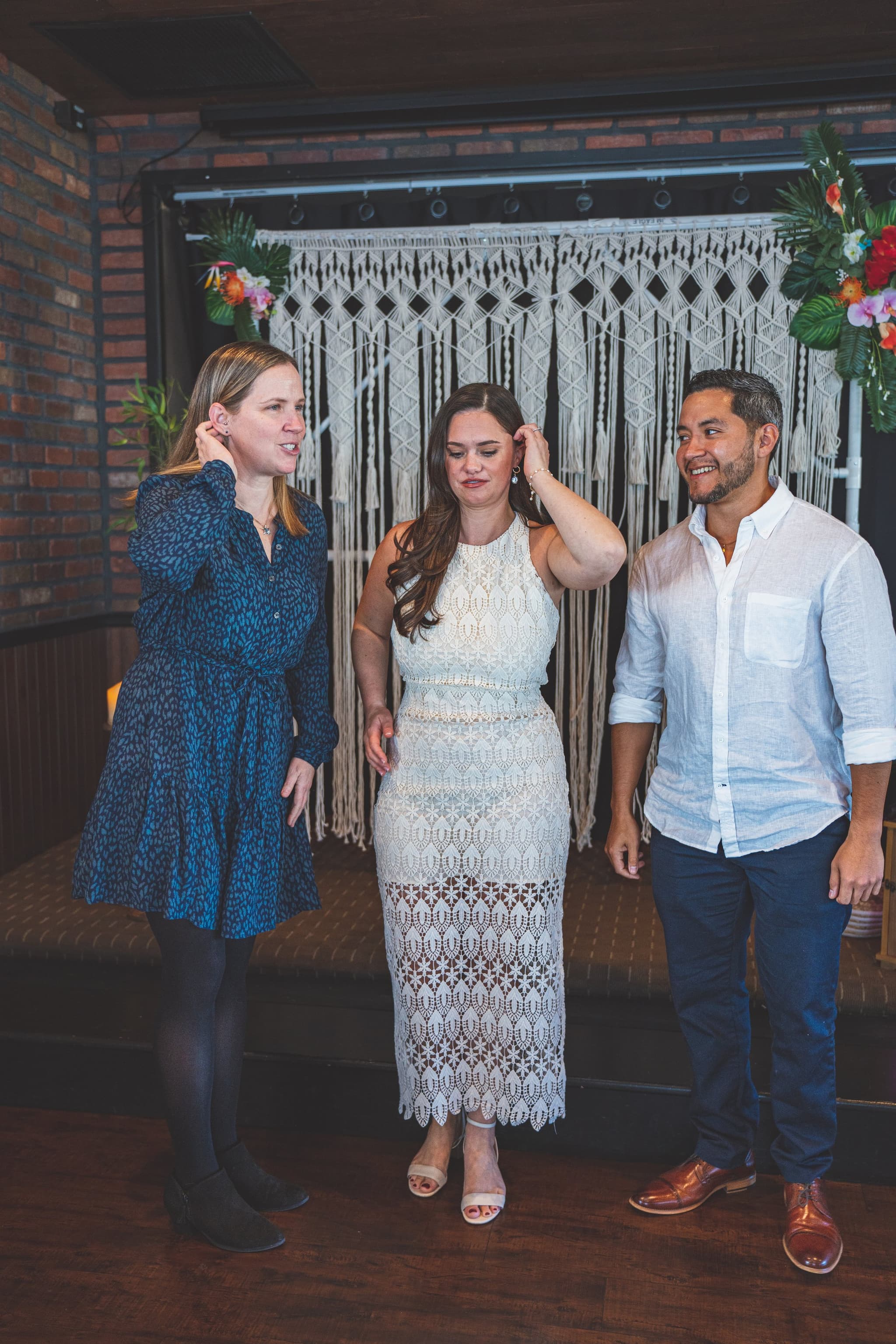 A candid moment of three guests laughing and adjusting their hair in front of the macrame backdrop