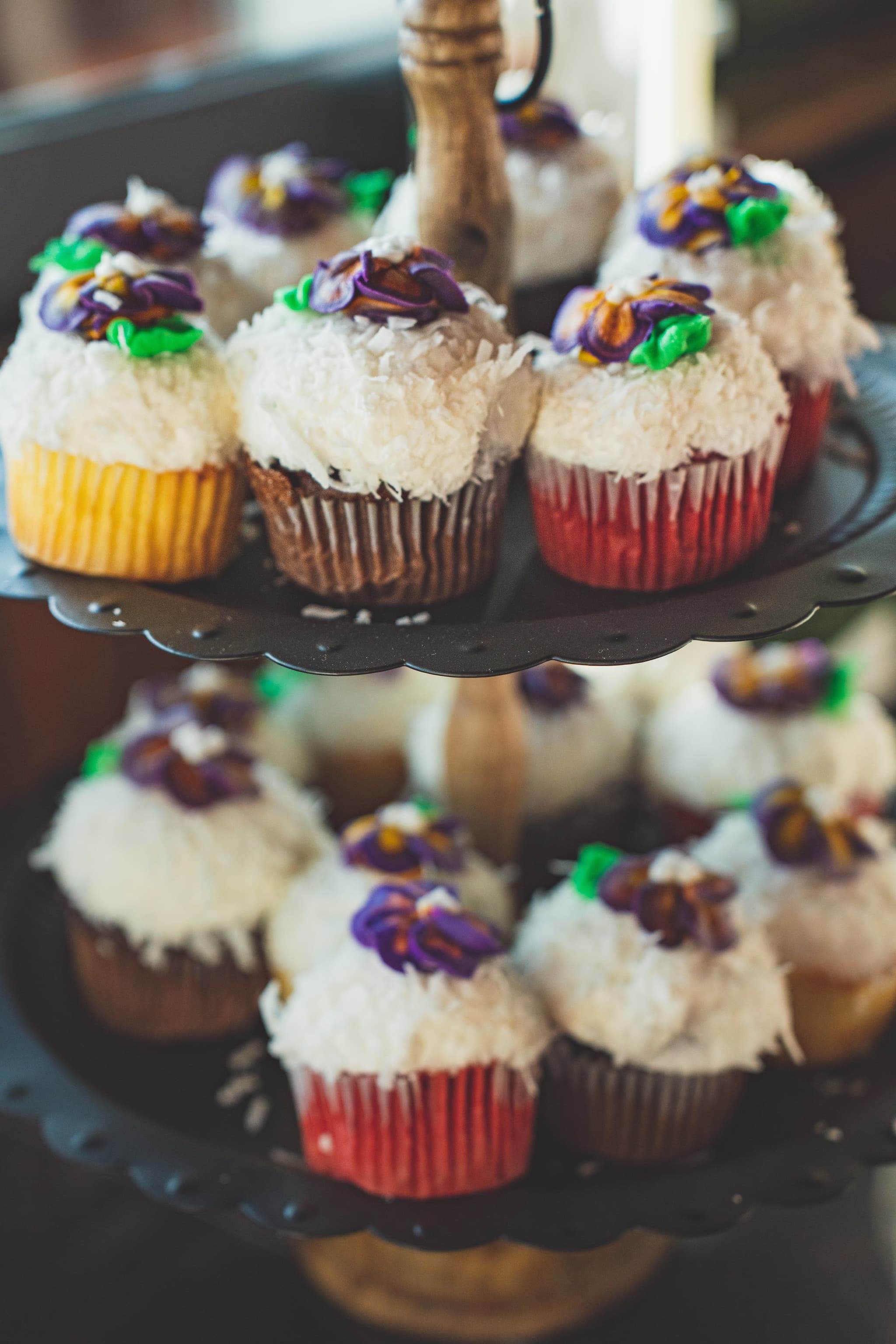 A close-up of a tiered dessert stand filled with coconut-frosted cupcakes decorated with colorful floral sprinkles