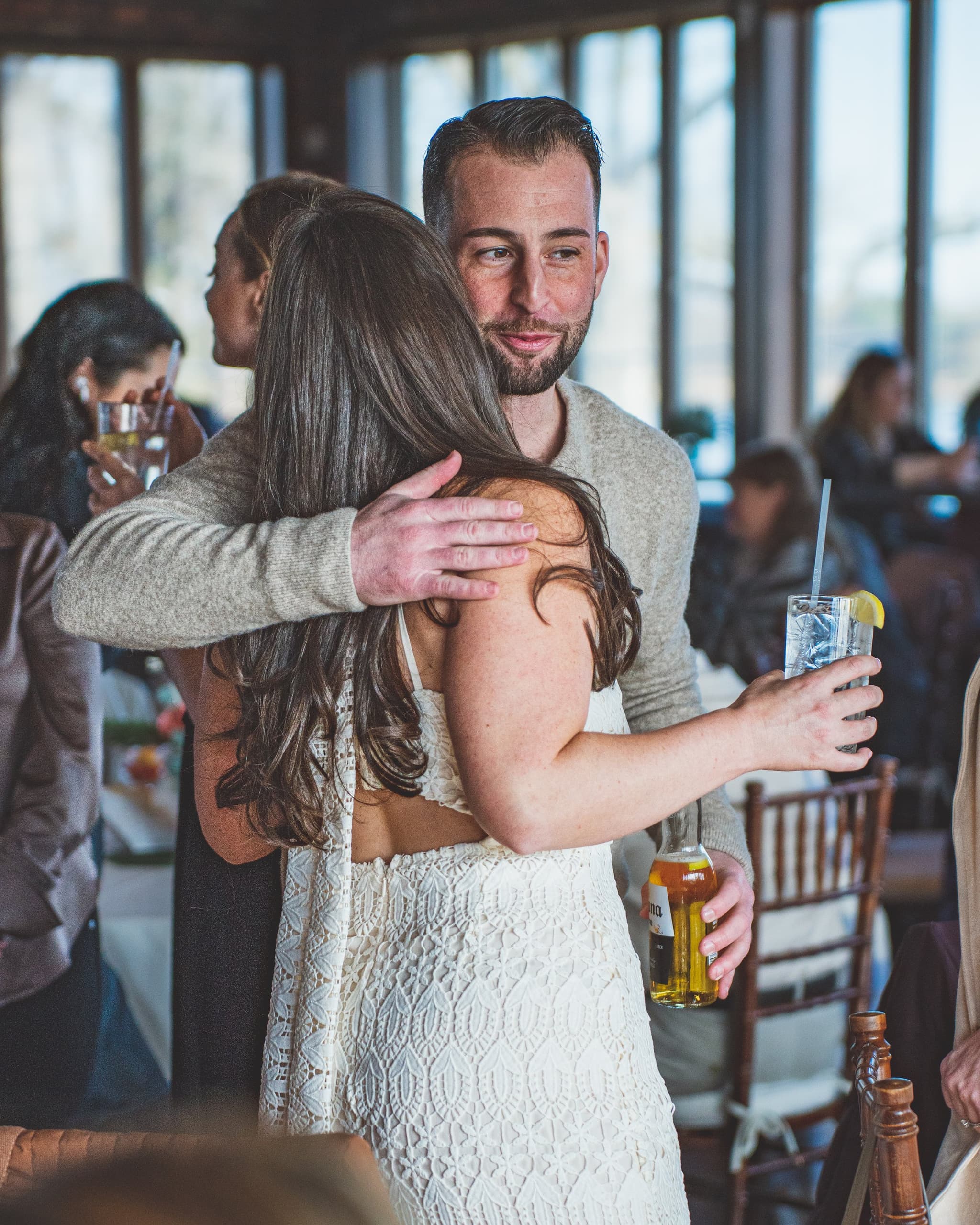 A candid moment of the bride-to-be embracing a male guest who holds a cocktail in the busy bridal shower venue