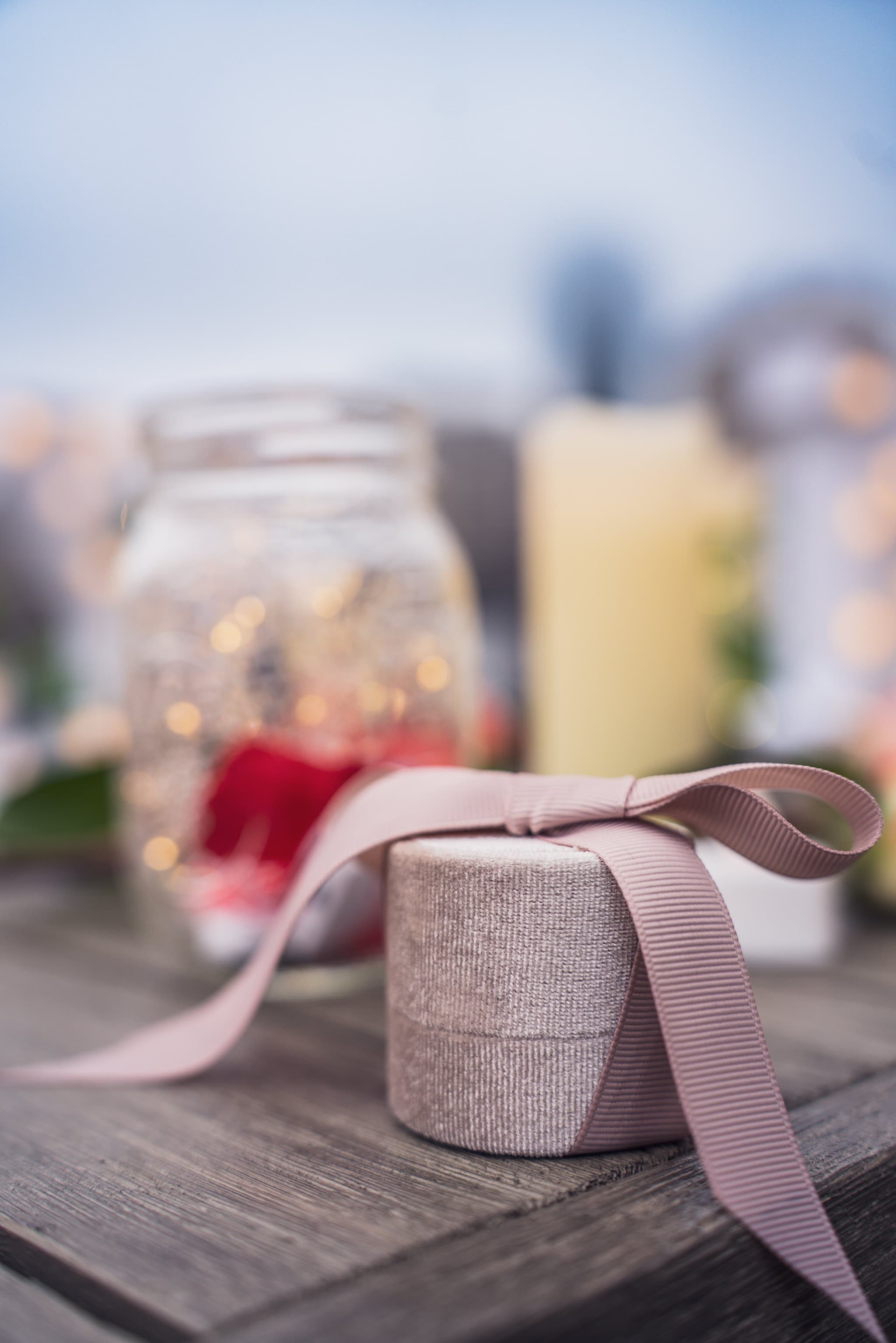 Ring box tied with pink ribbon with bokeh candles in background