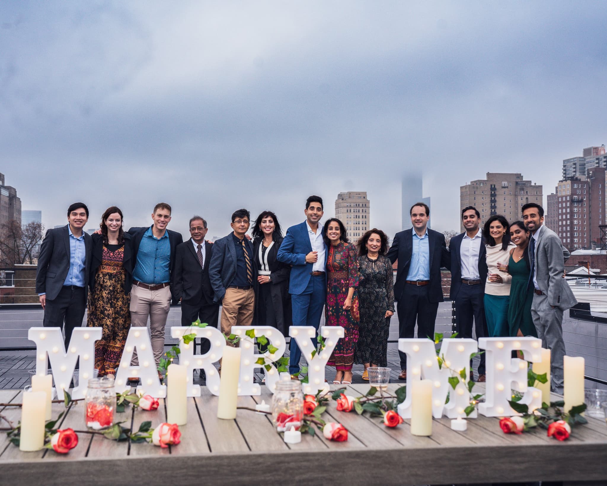 Group of guests surrounding couple at MARRY ME letters with cityscape
