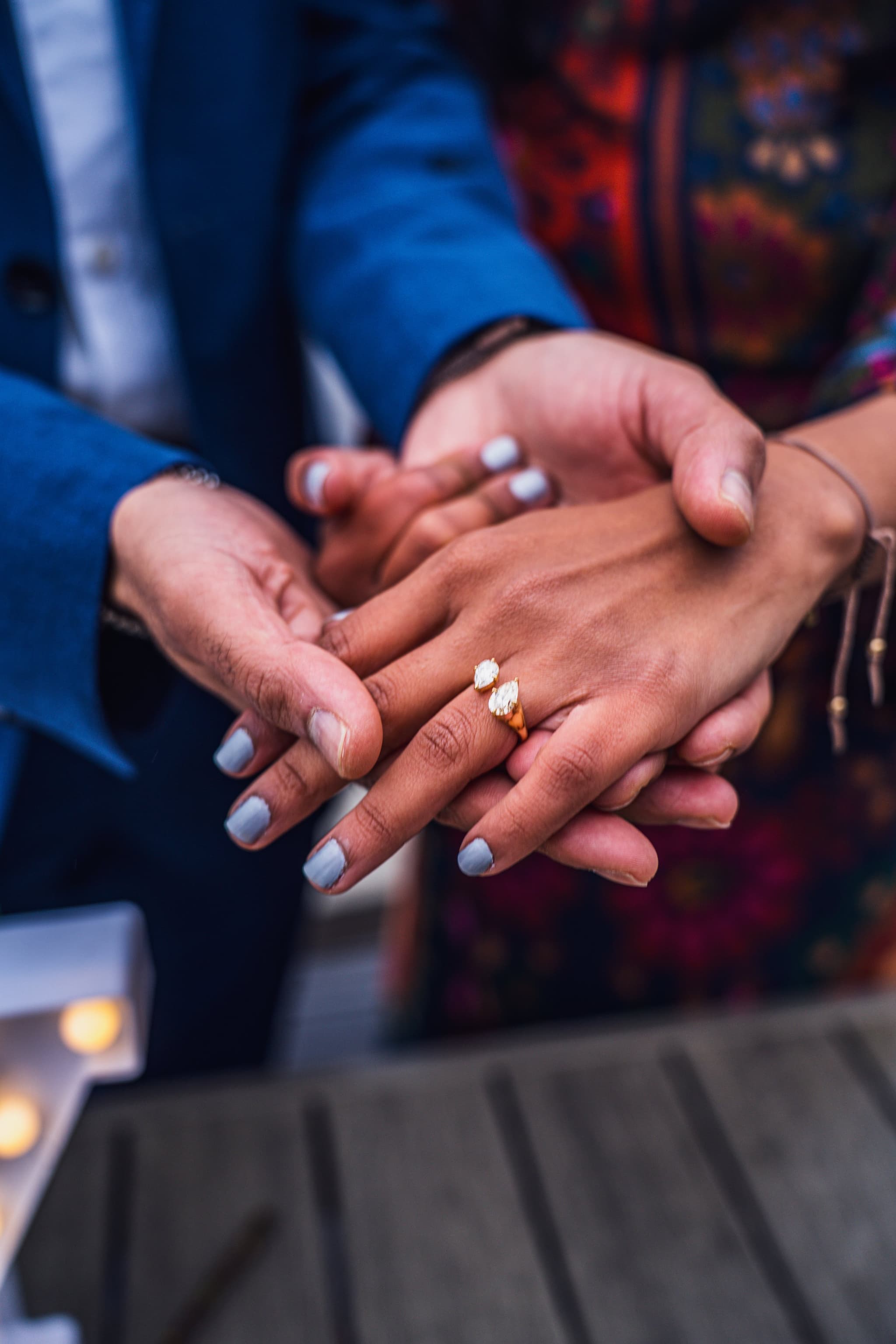 Close-up detail shot of the couple's hands stacked together showing off the diamond engagement ring with candlelight in the background