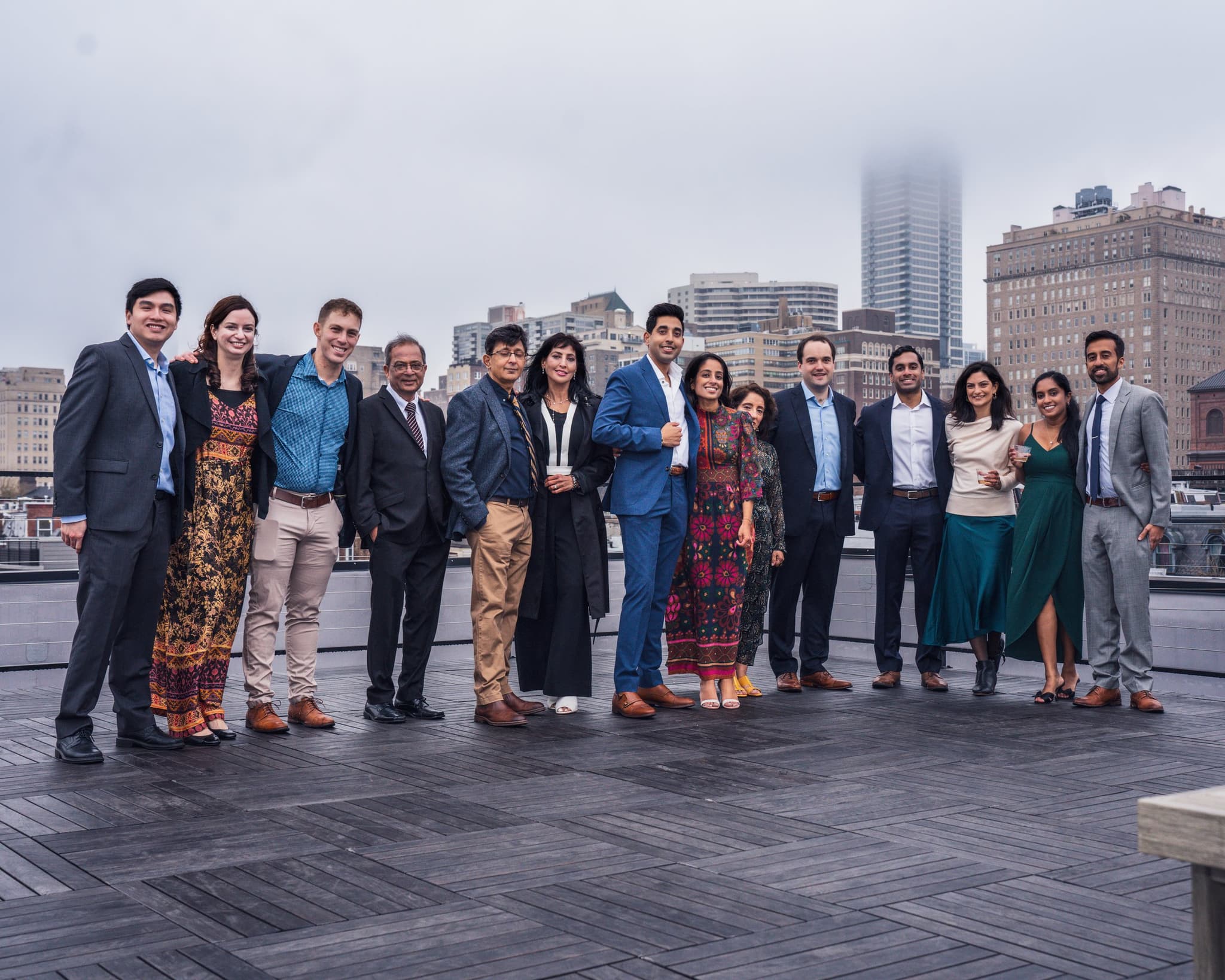 Large group of friends and family gathered on a rooftop terrace celebrating the engagement with the city skyline stretching behind them