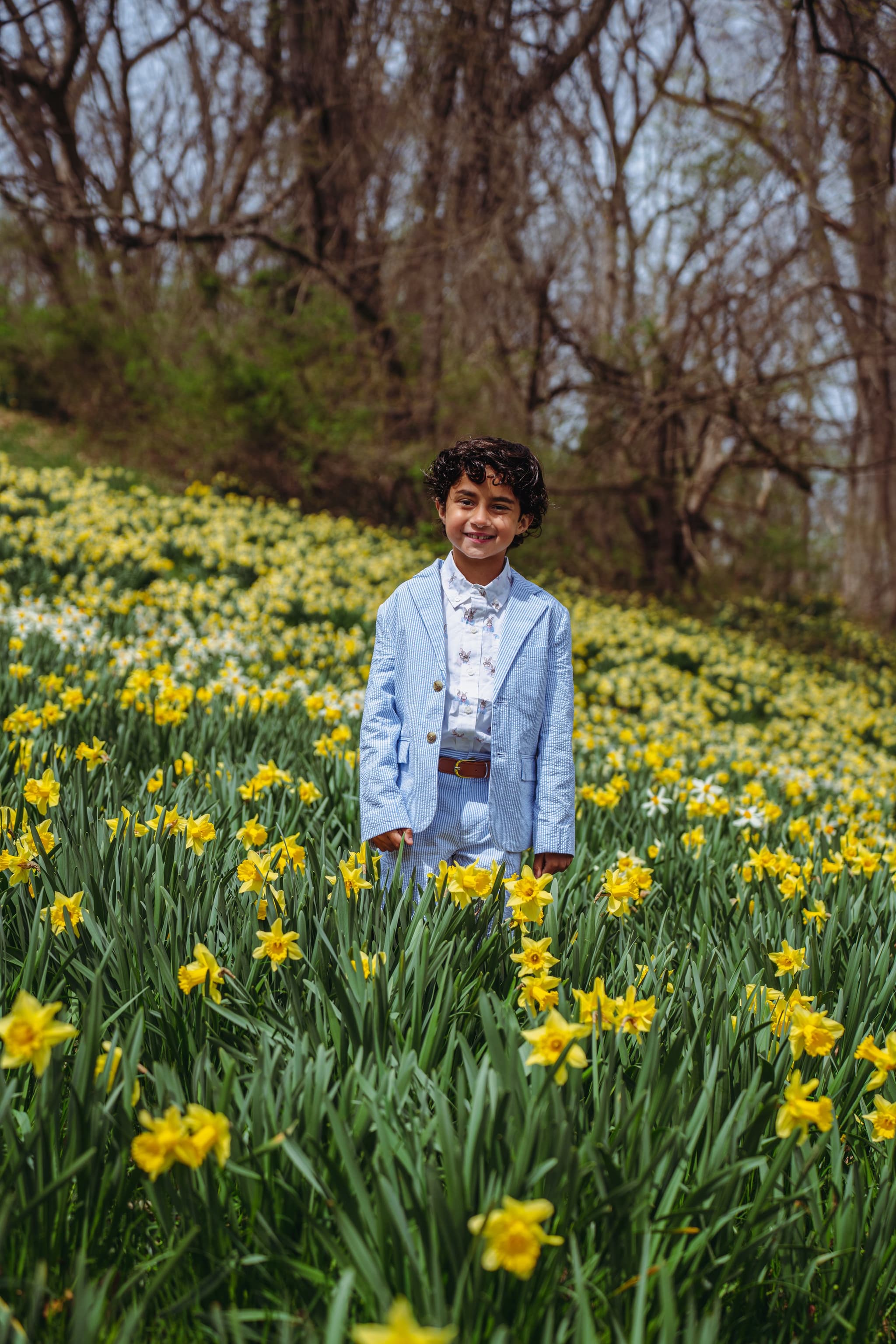 Boy in blue linen suit standing in a field of yellow daffodils, smiling