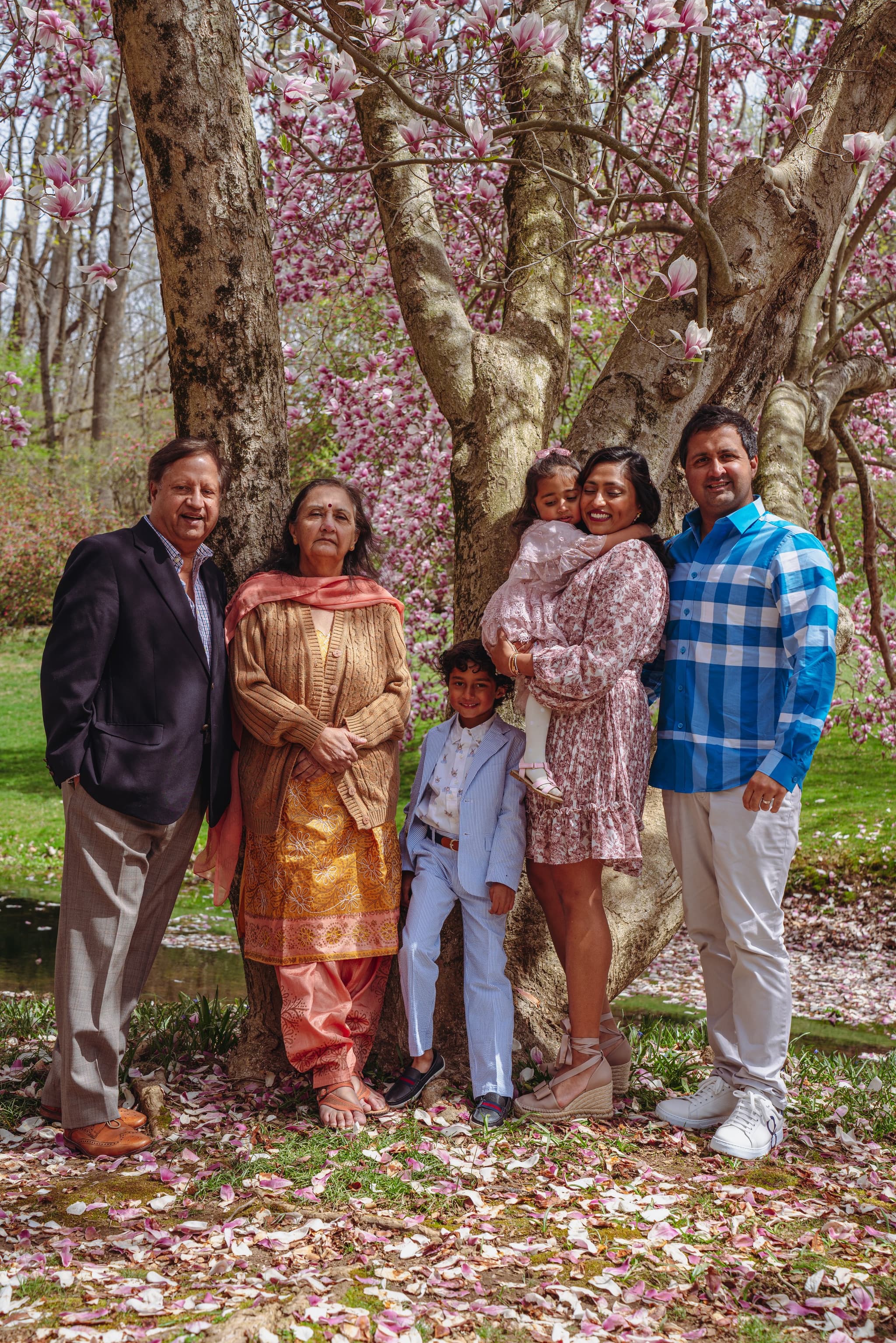 Extended family group portrait under magnolia tree with pink petals on ground