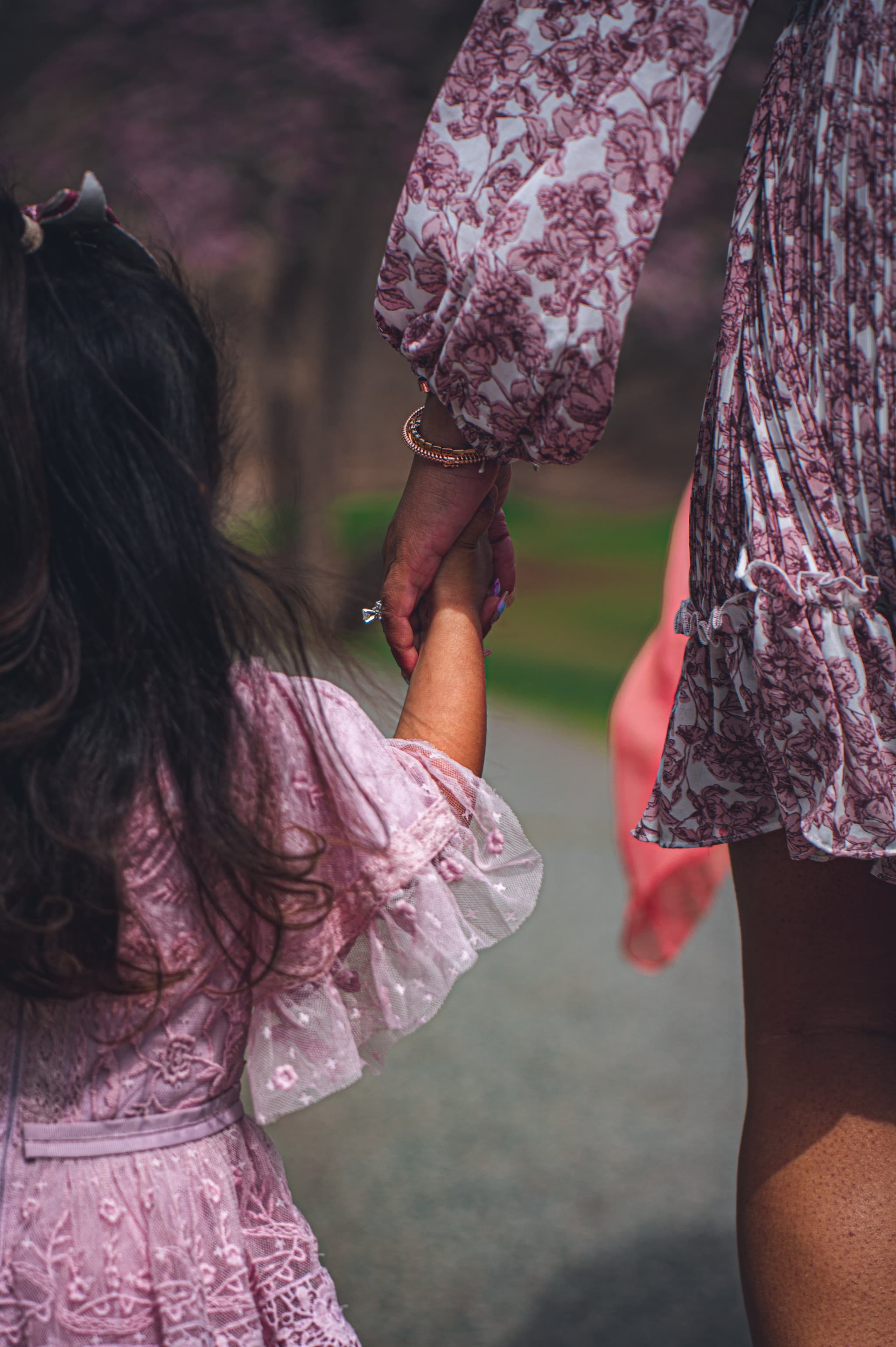 Close-up of mother and daughter holding hands while walking in the park