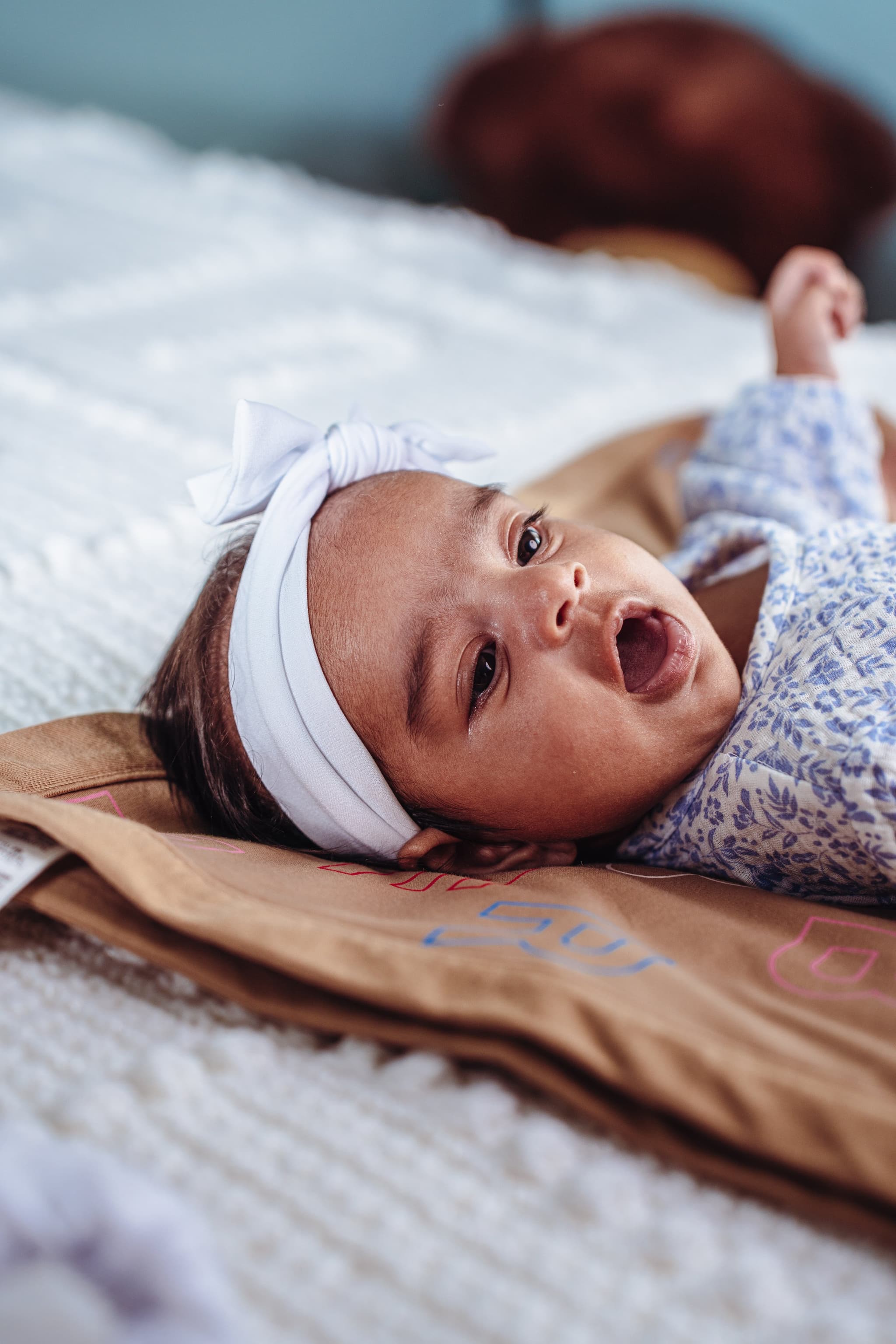 Newborn baby girl in floral romper with white bow headband, alert and looking up