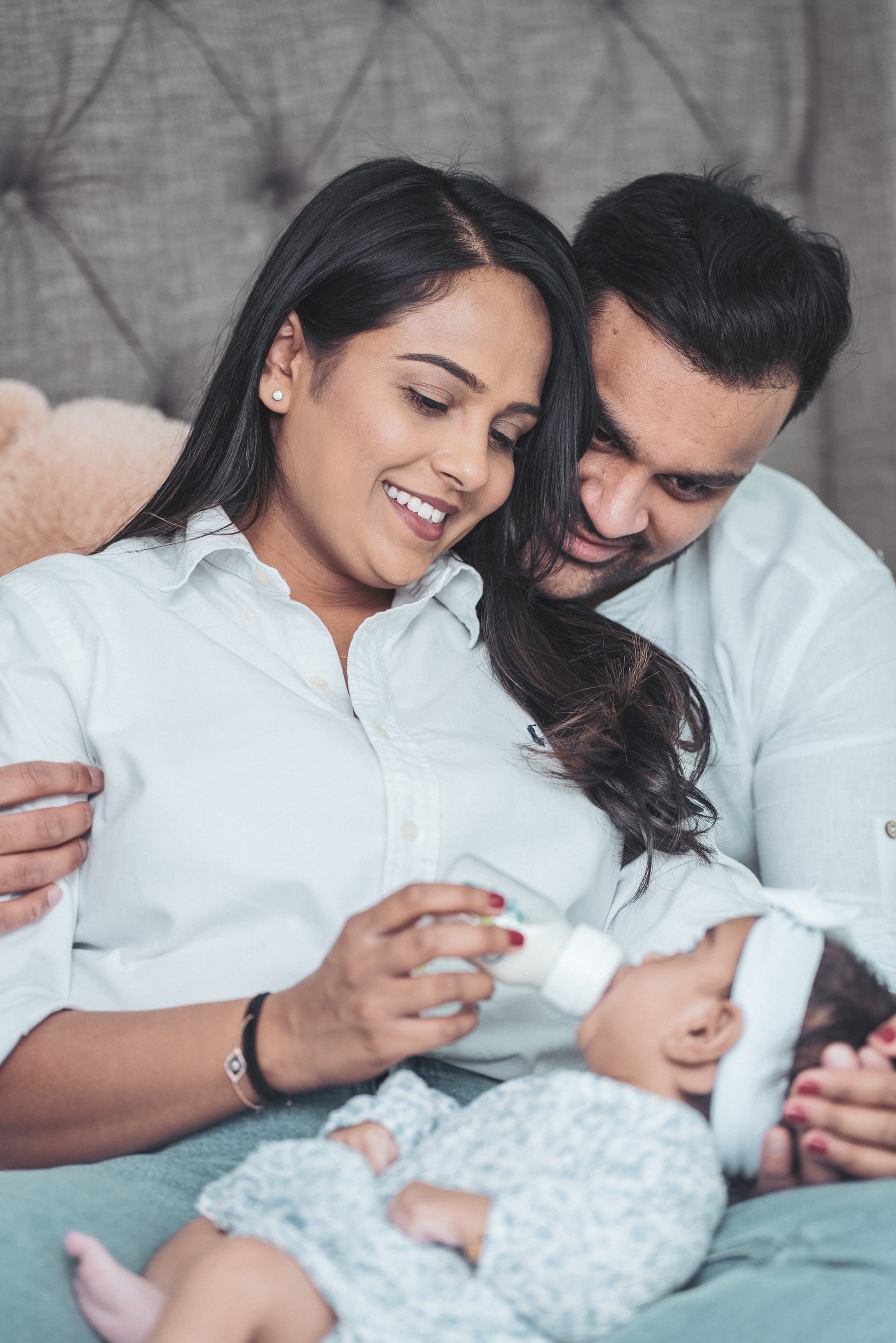 Mother and father smiling warmly as they hold their newborn baby together