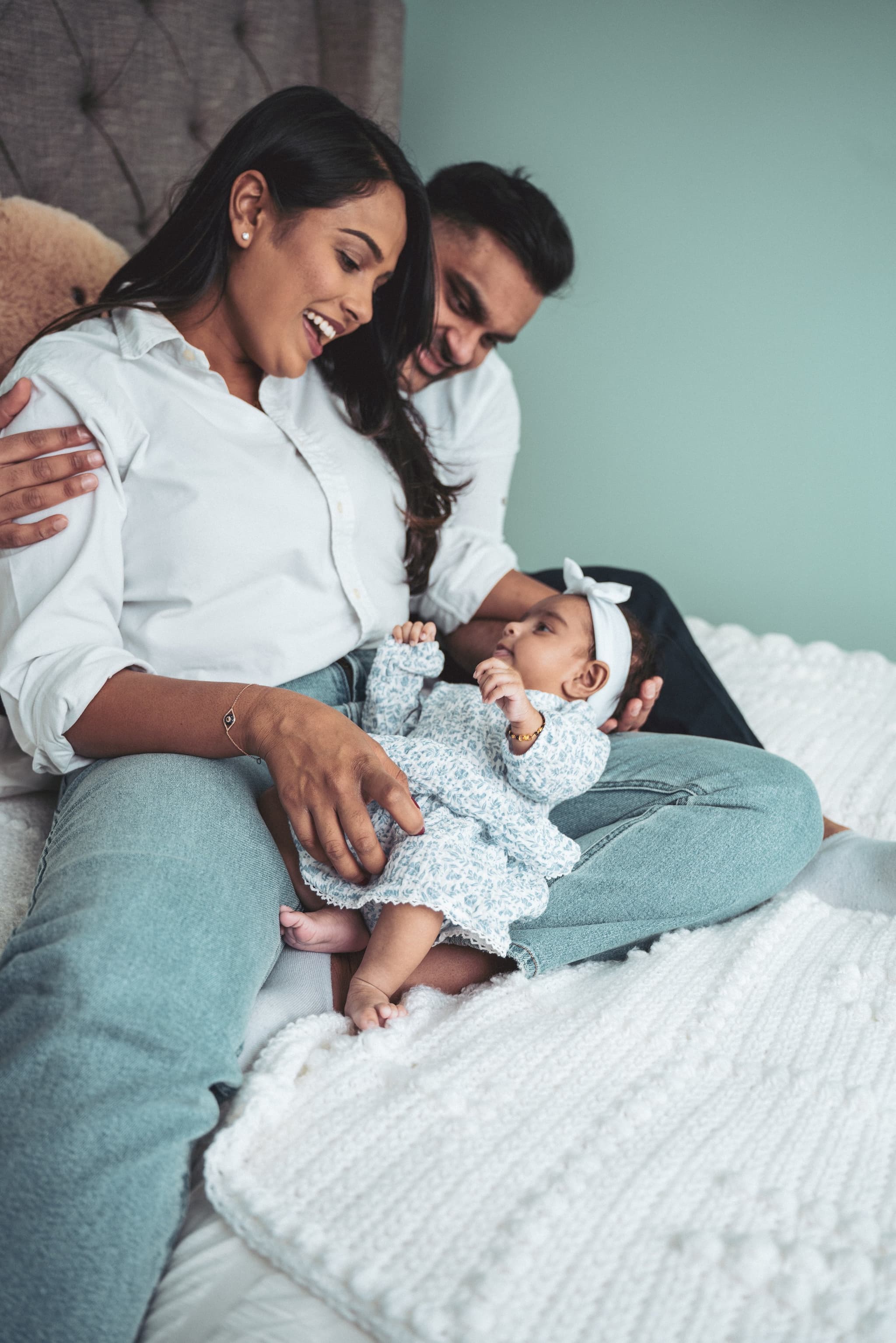 Parents sitting on the bed together, joyfully looking at their newborn in mama's arms