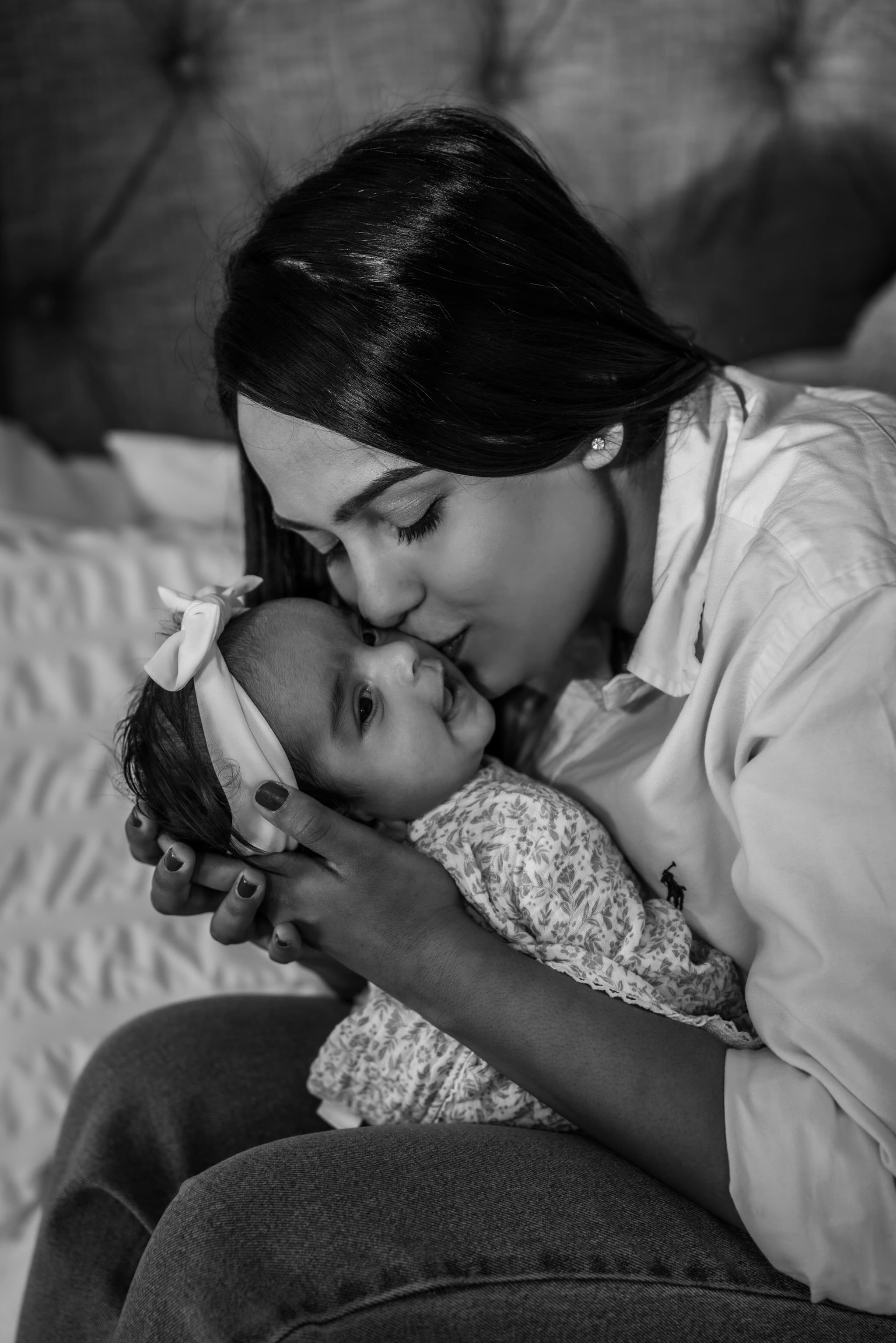Black and white portrait of mother tenderly kissing her newborn baby girl