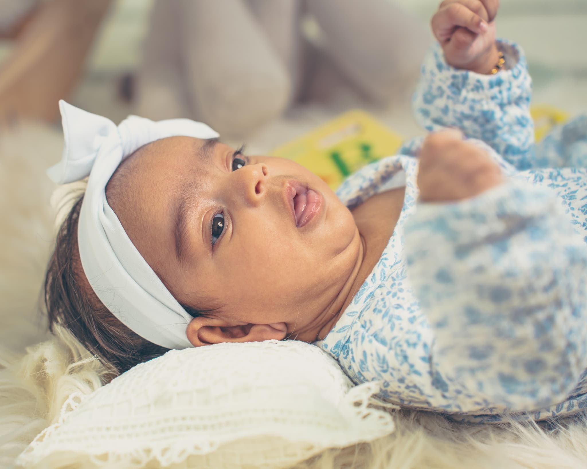 Close-up of newborn baby's face and tiny raised fist on a soft fur rug