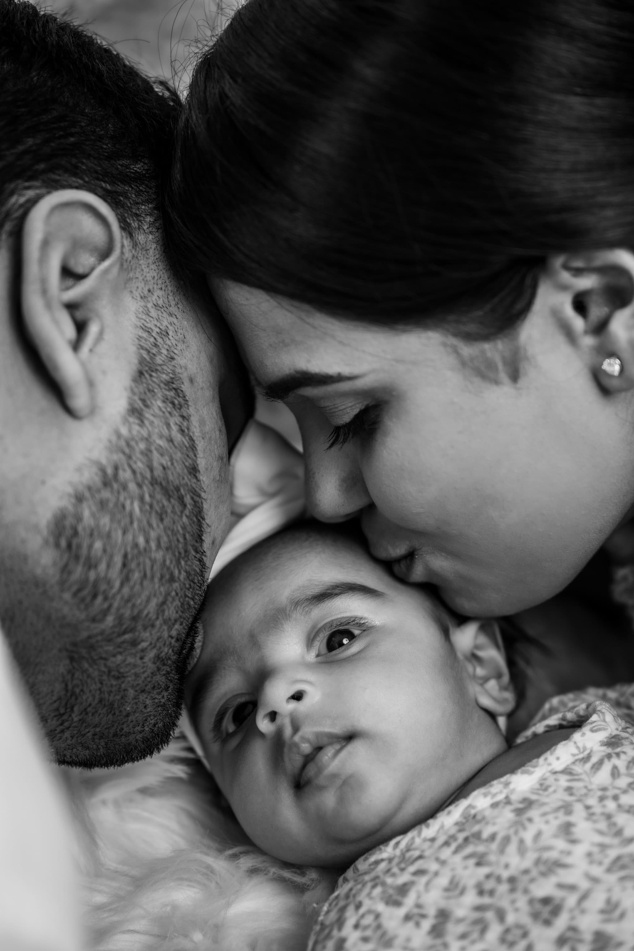 Black and white close-up of parents leaning in to kiss their newborn from both sides