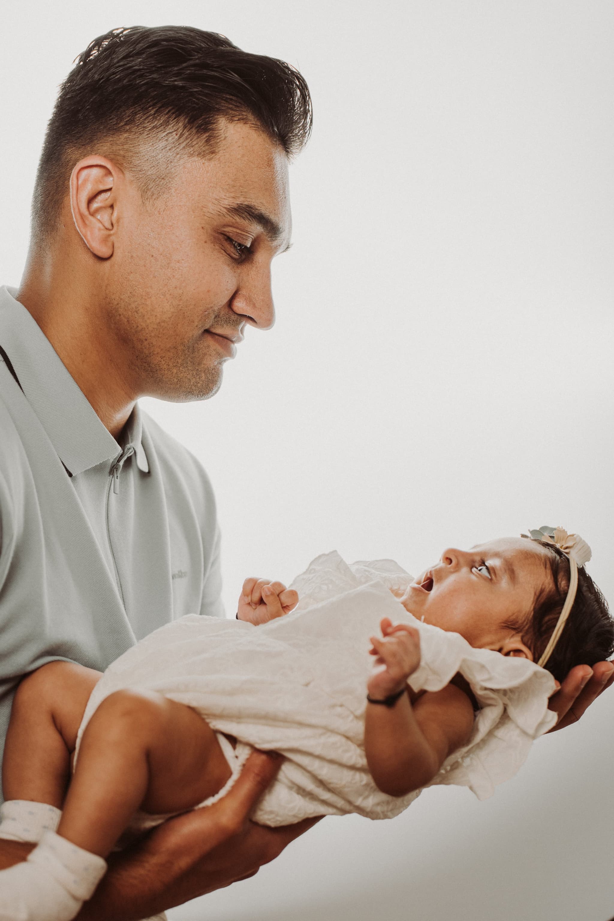 A father gazes lovingly down at his newborn daughter cradled in his arms against a clean white background