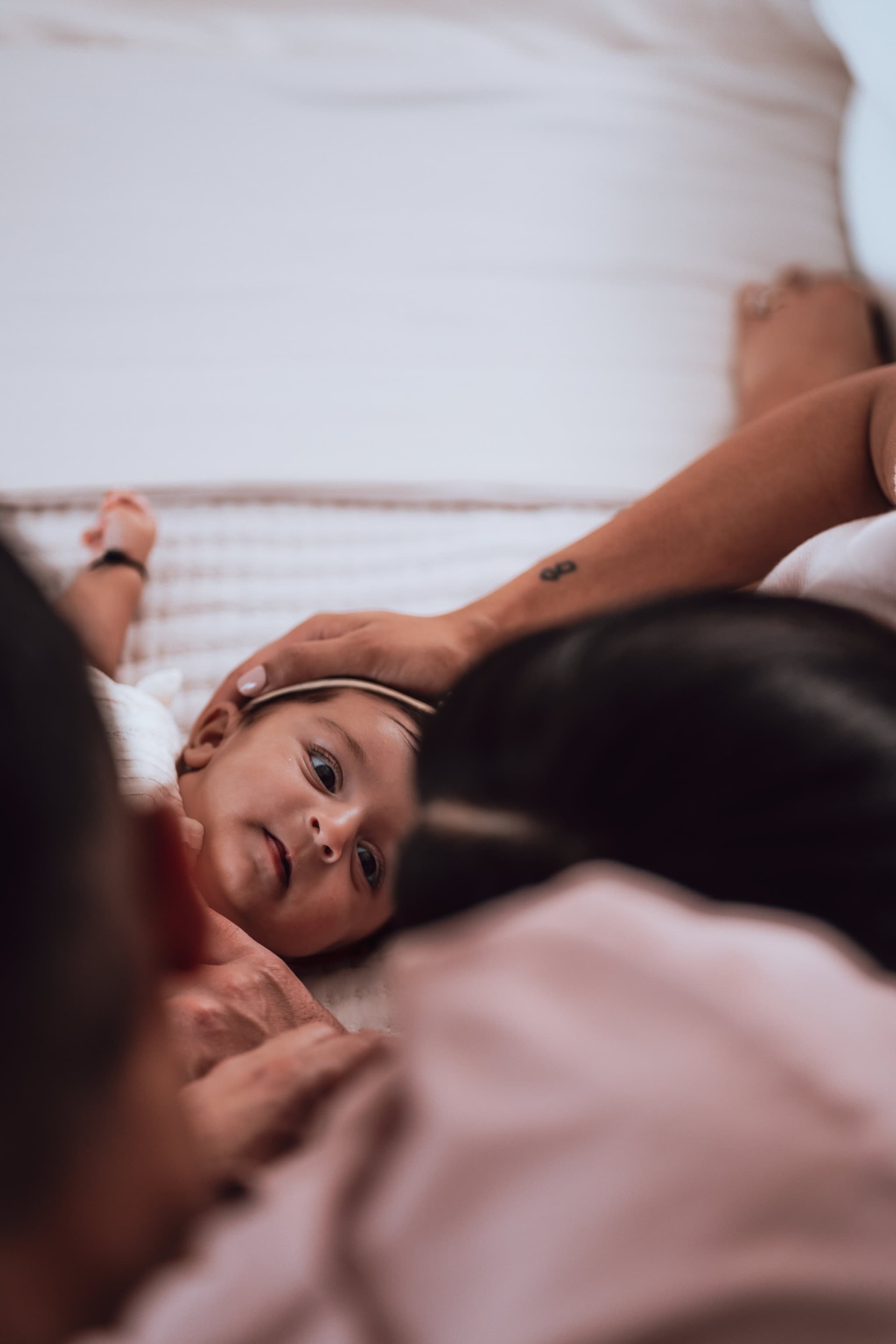 A close-up portrait of a wide-eyed newborn baby girl lying between her parents' gentle hands