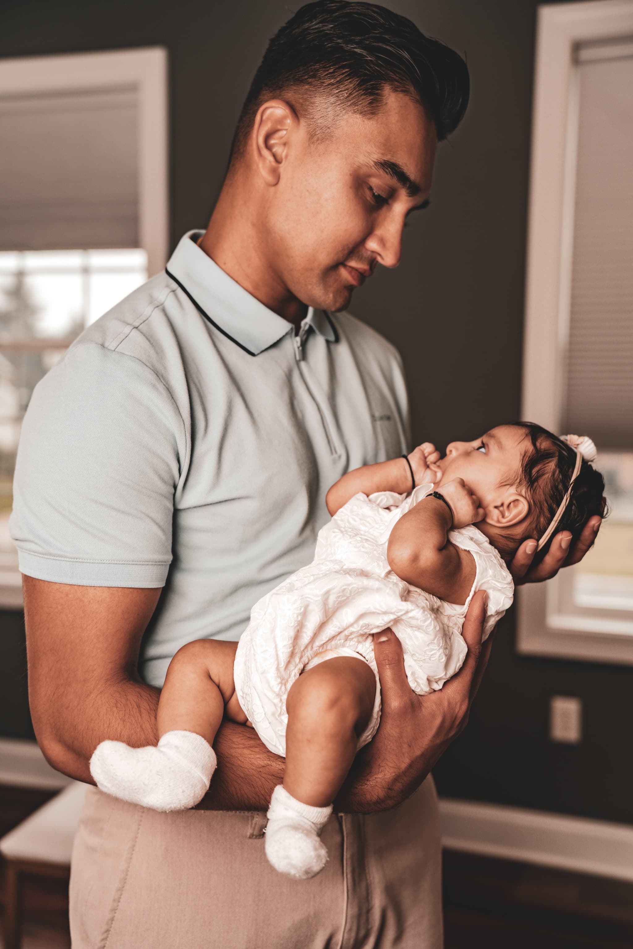 Newborn baby girl dressed in a delicate white outfit resting peacefully in a parent's gentle arms