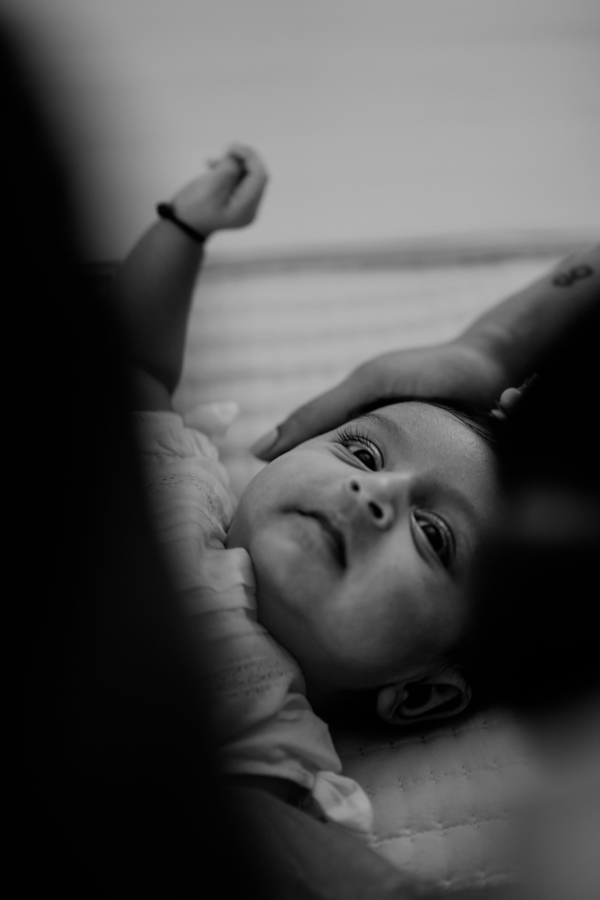 Mother gazes down at her newborn with pure adoration, soft window light illuminating both faces