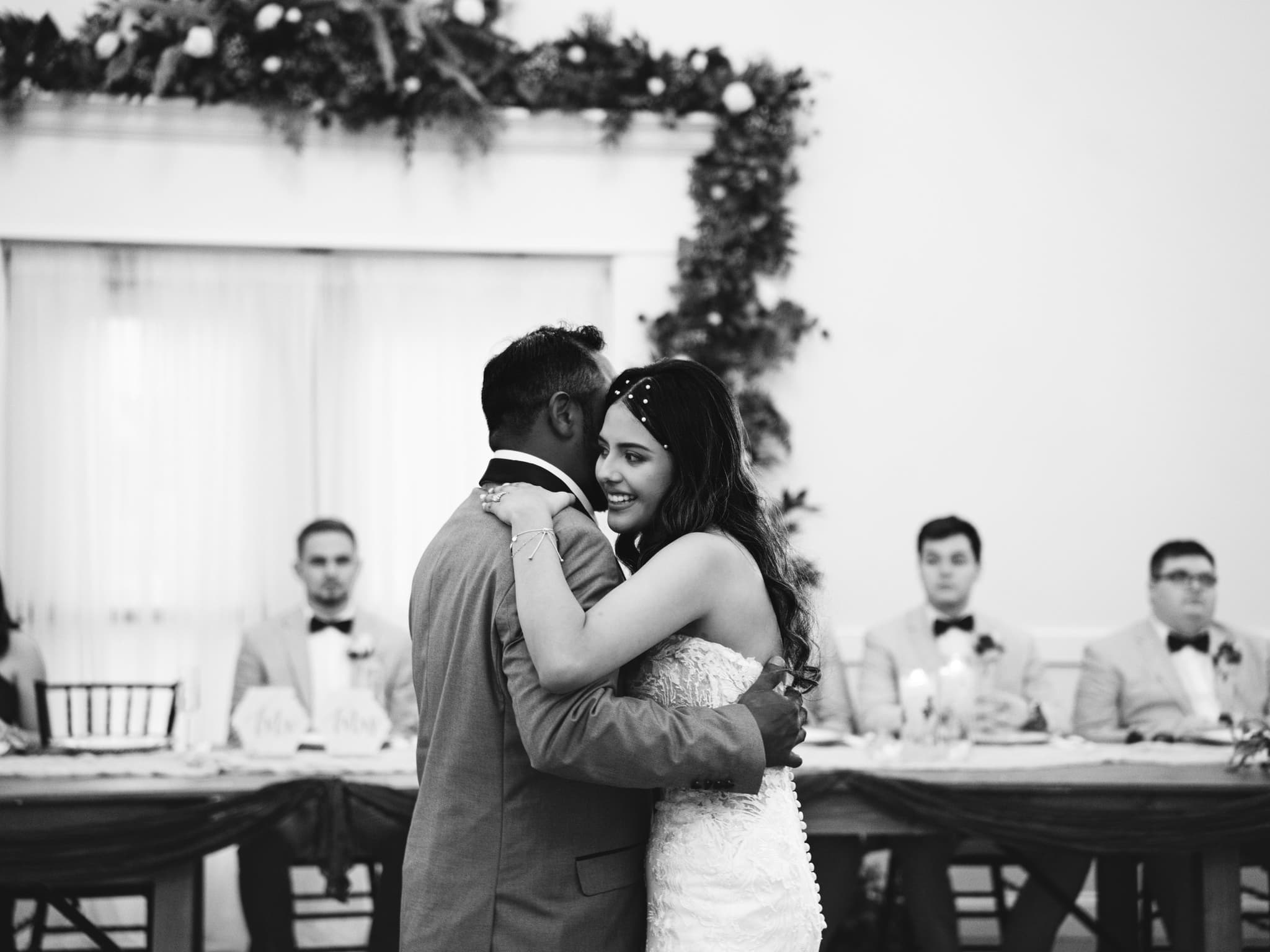 Black and white first dance — bride radiant smile while guests look on