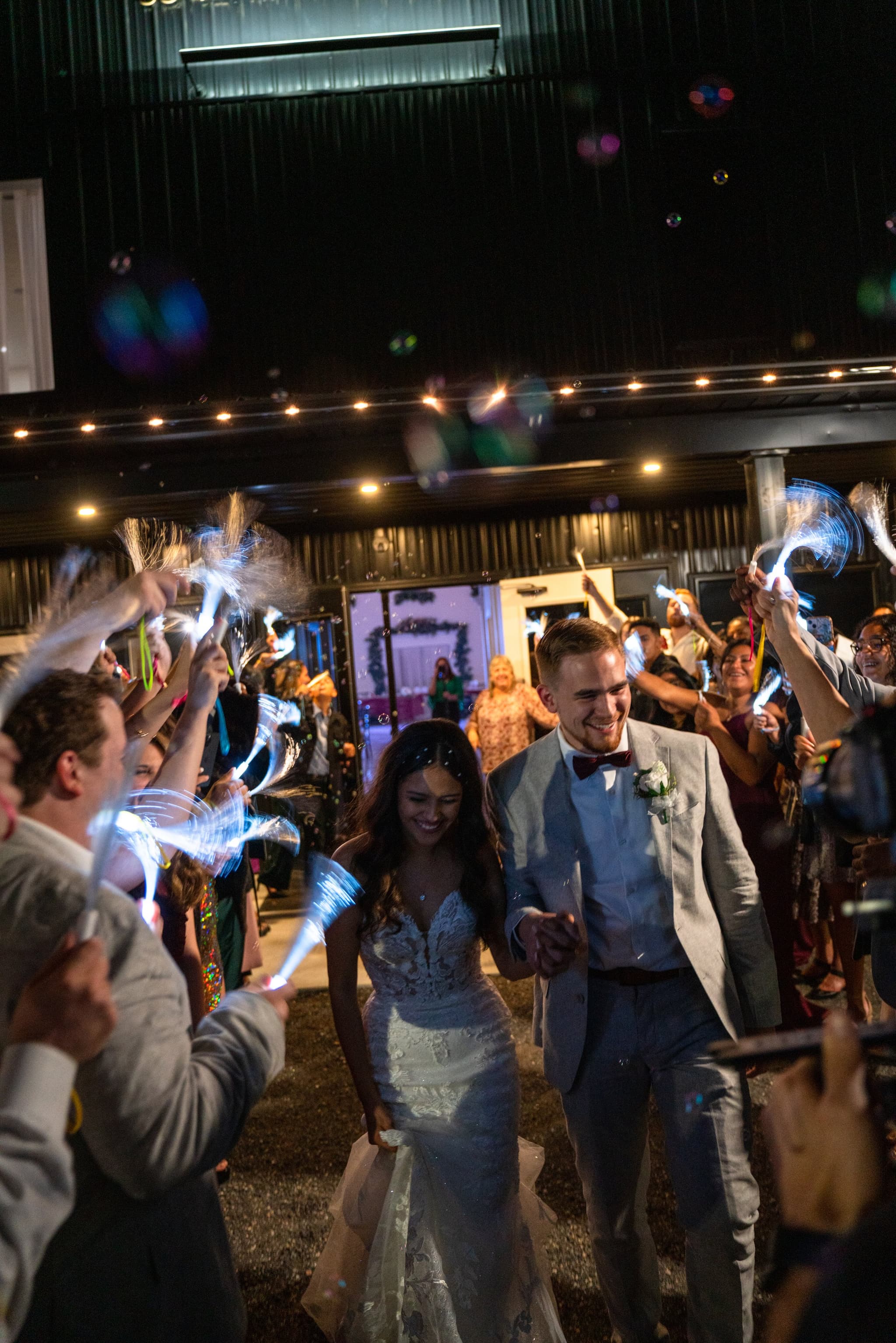 Joyful grand exit — couple running through a tunnel of glowing wands and bubbles