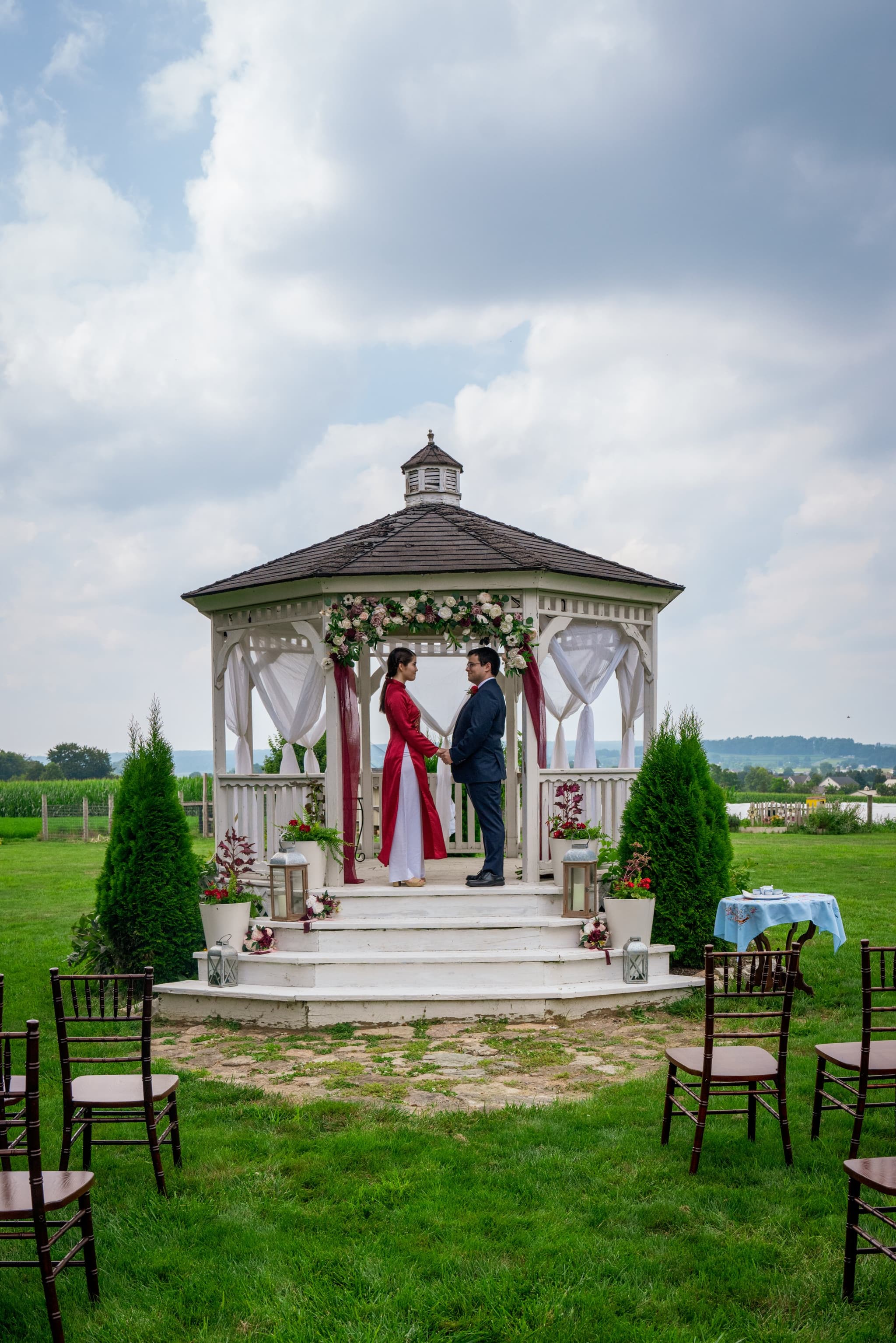 Bride and groom face each other beneath a flower-adorned white gazebo during their outdoor ceremony