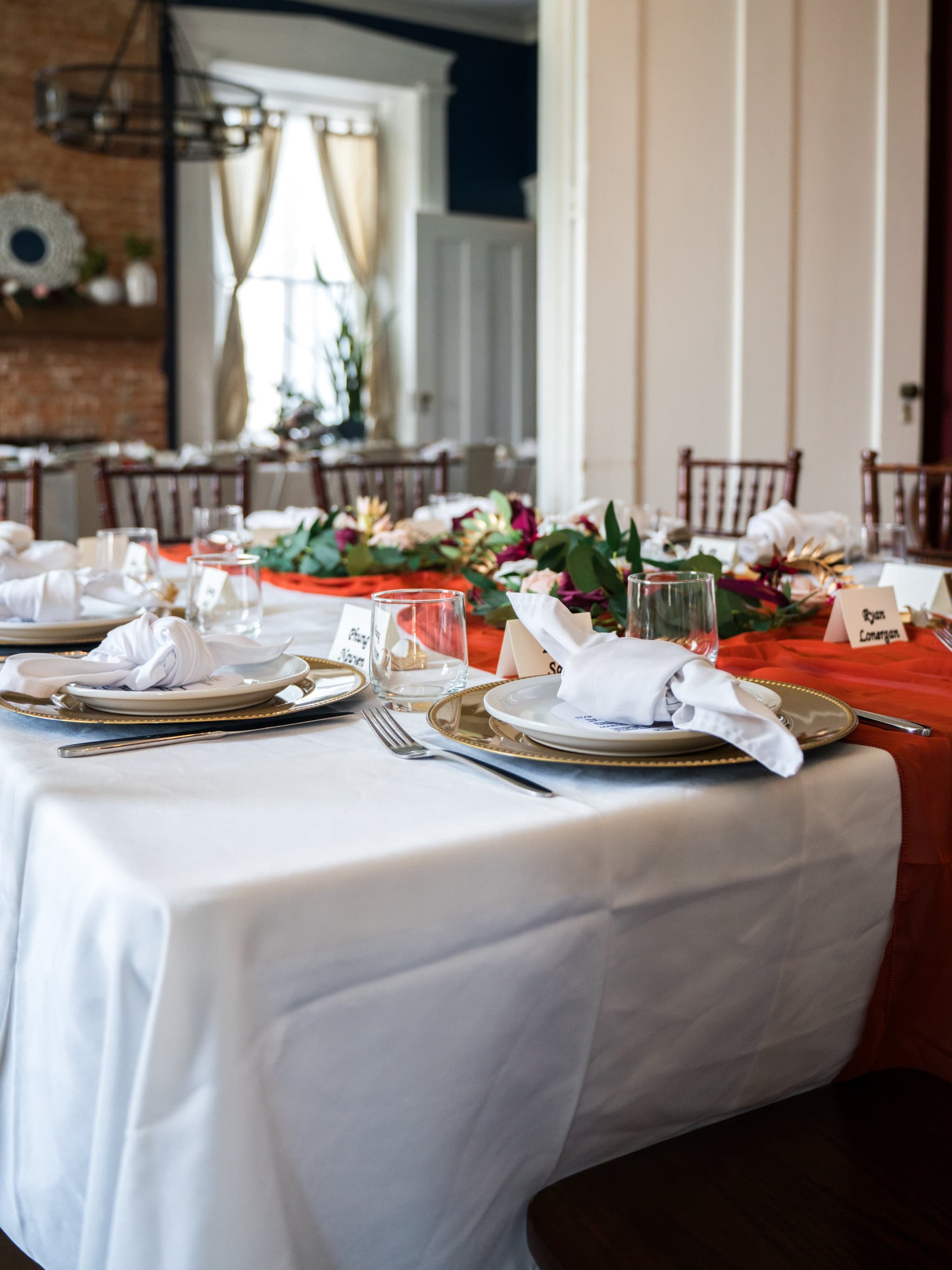 Elegantly set reception dinner table with gold charger plates, folded linen napkins, glassware, and a lush floral centerpiece