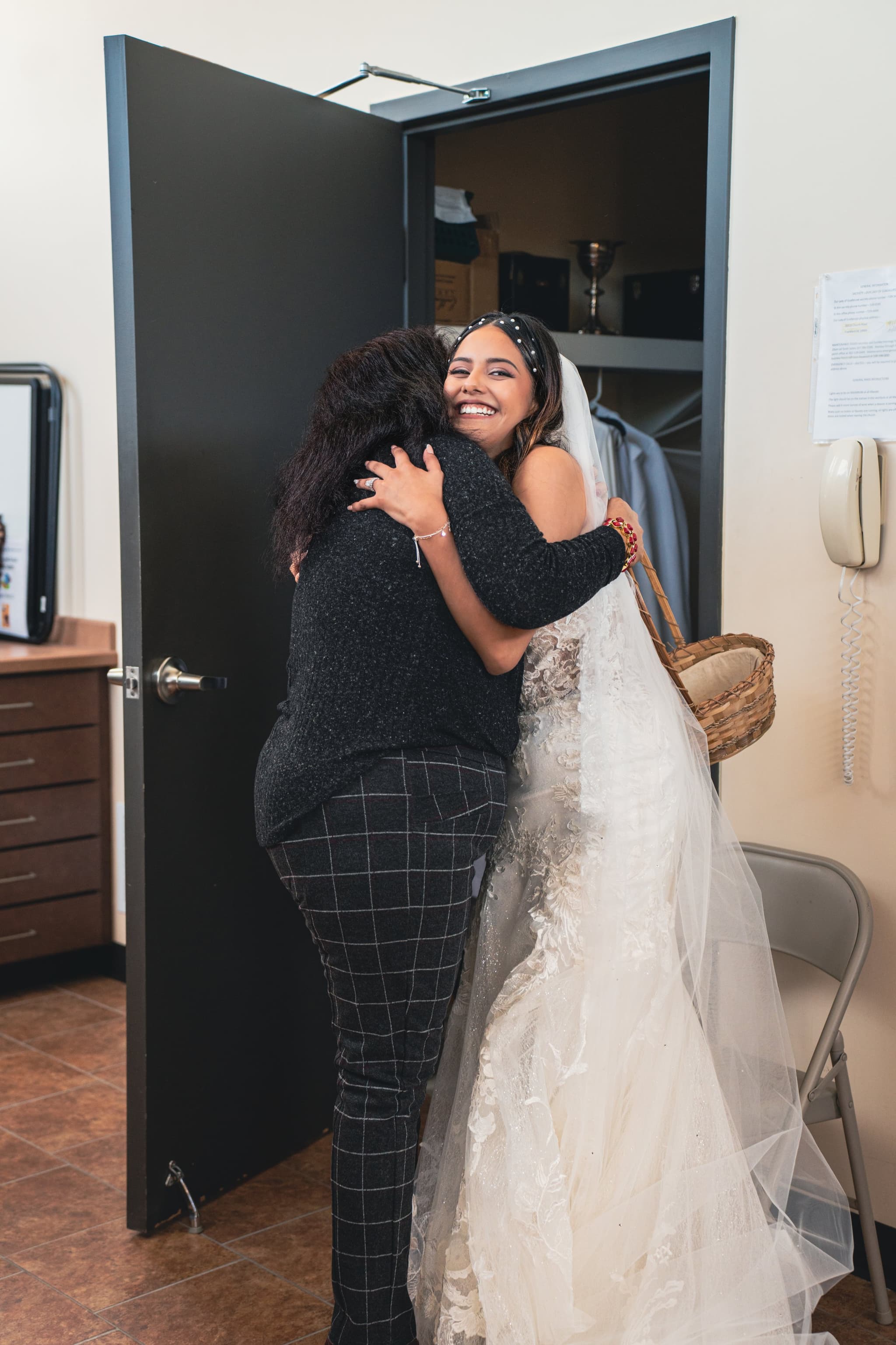 The bride in her lace gown shares a joyful embrace with a guest, her beaming smile capturing a candid moment of emotion before the ceremony