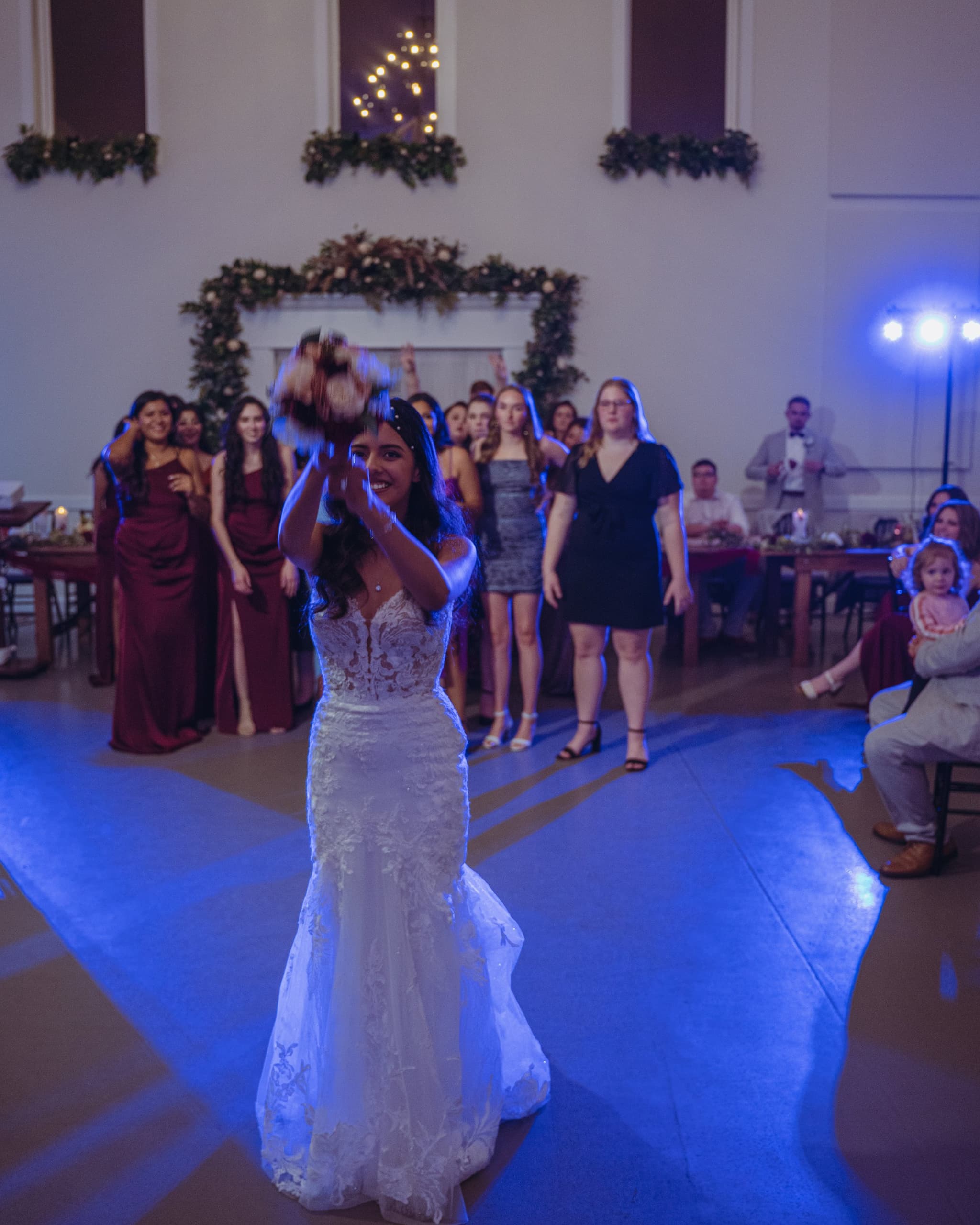 The bride launches her bouquet toward eager guests on the dance floor during the bouquet toss under vibrant blue reception lighting